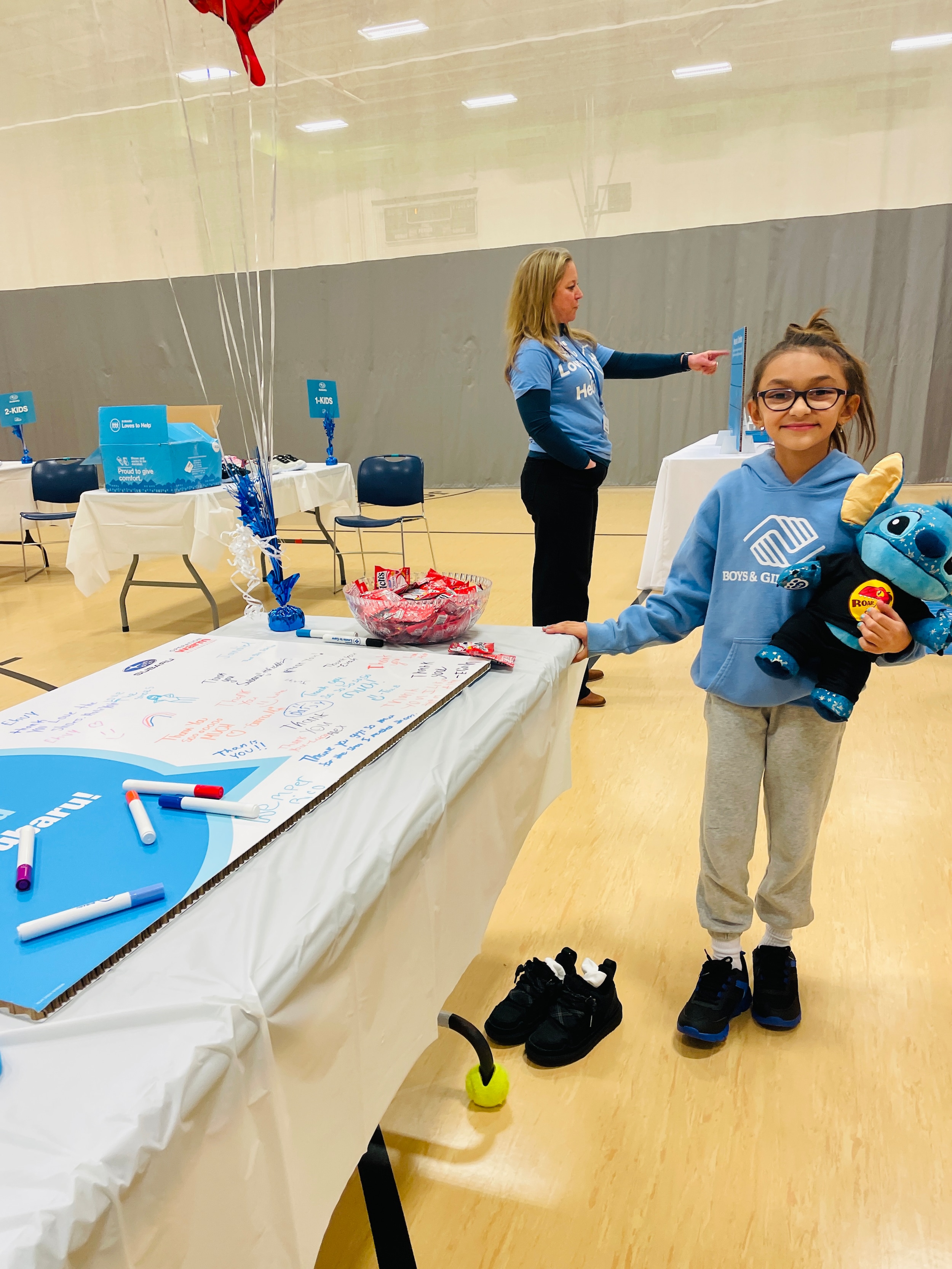young girl with a pony tail in a blue BGCWD sweatshirt holding a stich stuffy wearing her new shoes