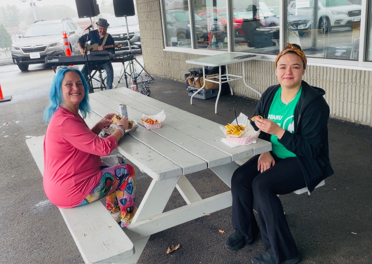 2 women sitting on a bench with food from soulfully vegan while listening to live music 