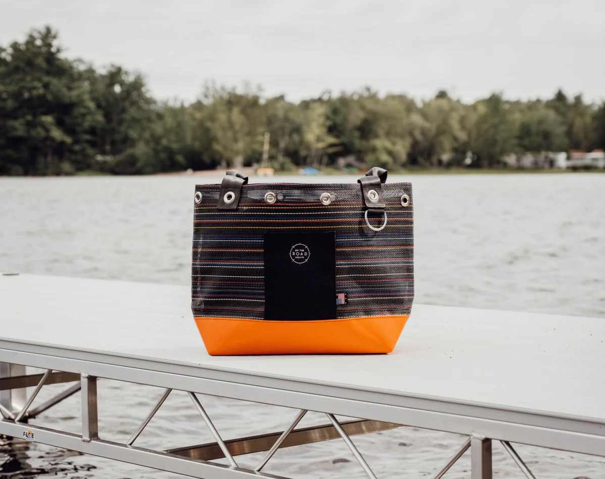 black bag with an orange bottom sitting on the dock in front of the ocean and trees
