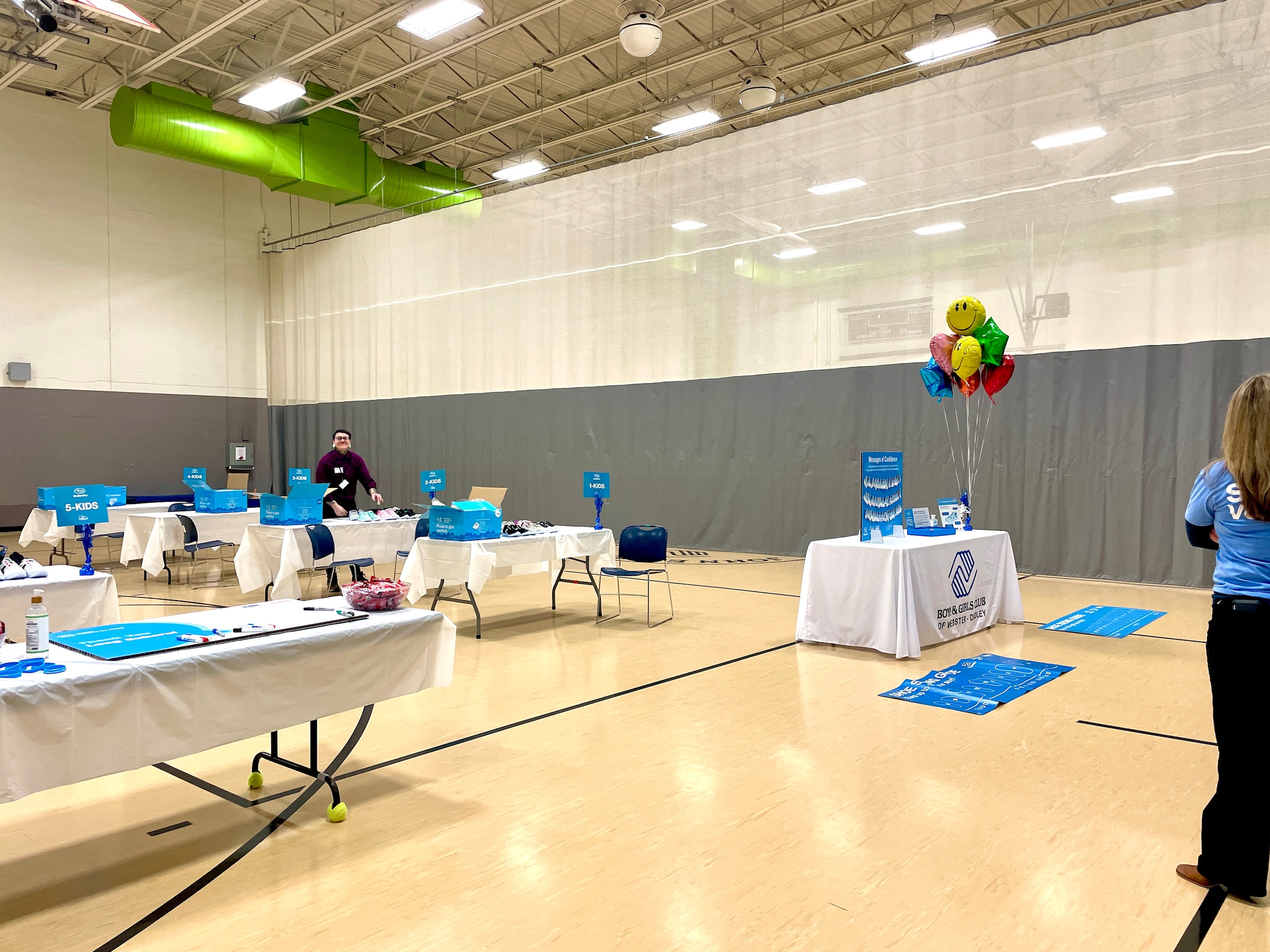 a bright school gymnasium with tables set up and colorful balloons at the sign in table.