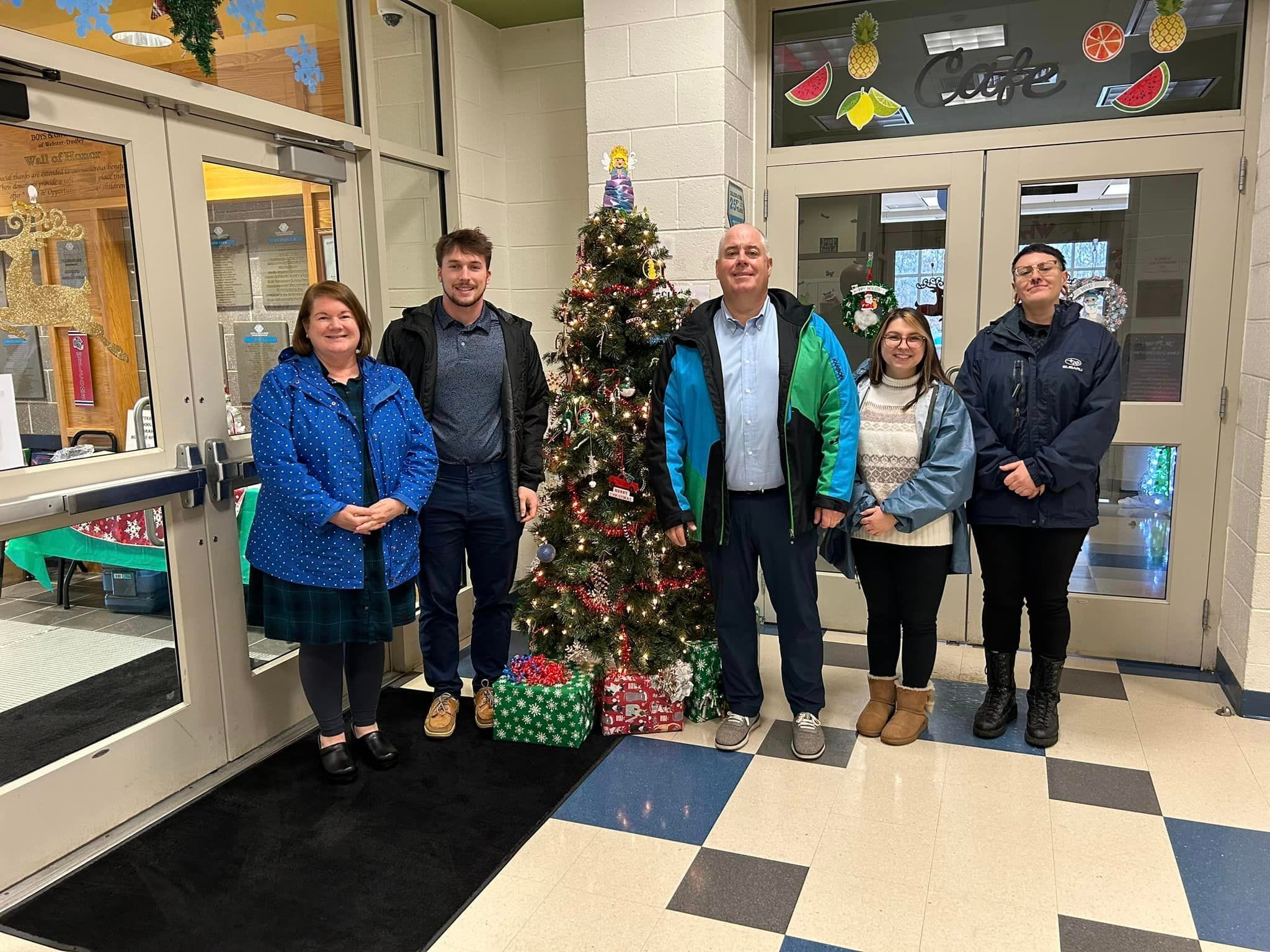 5 Subaru employees standing next to a Christmas tree with presents underneath