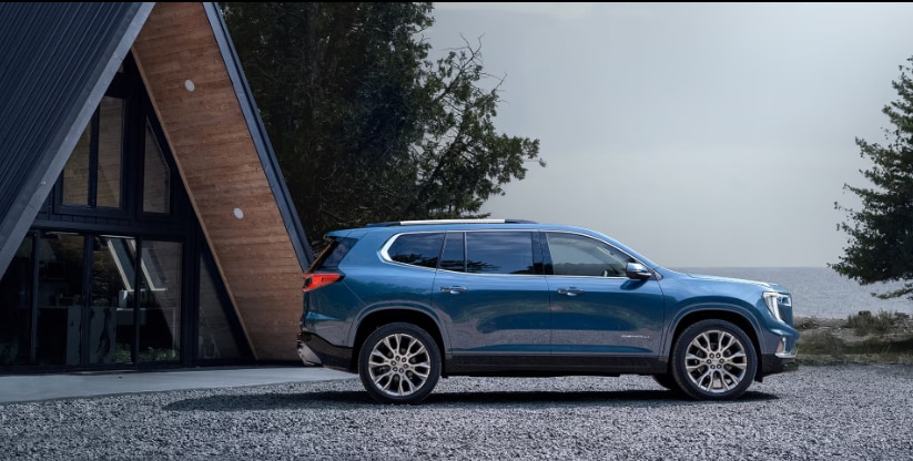 Side view of a blue GMC Acadia Denali parked in front of a modern cabin available at Lunghamer Buick GMC.