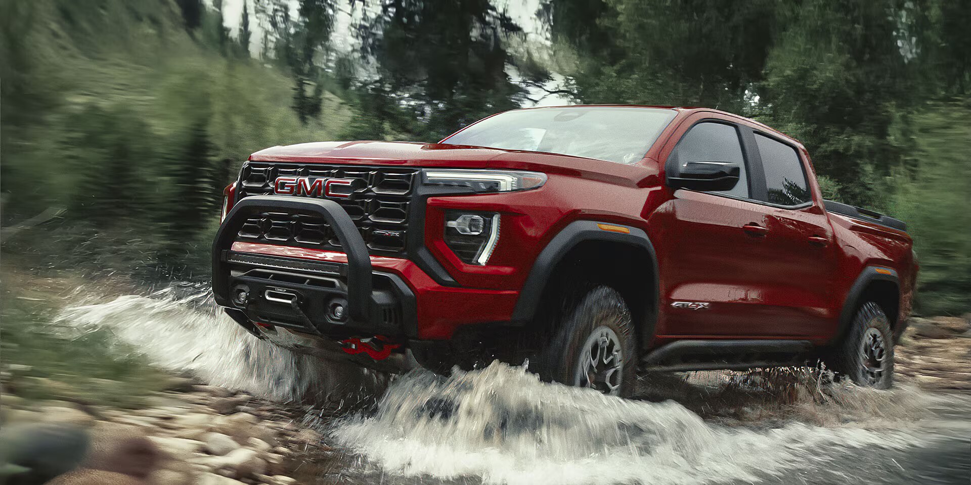 Bergundy 2026 GMC Canyon drivng over large boulders.