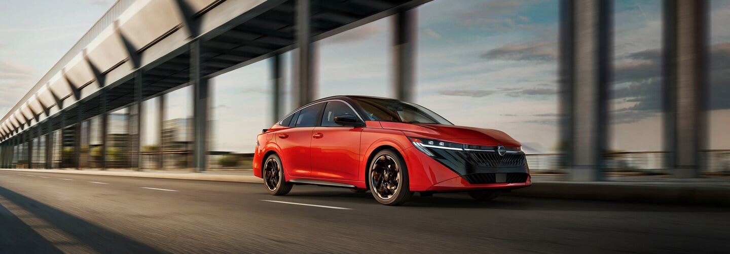 New Nissan Vehicles for Sale Red Nissan sedan driving on a city roadway near a modern architectural structure