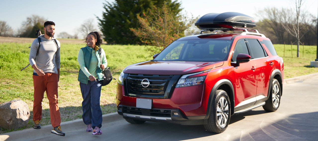 Used and Certified Pre-Owned Vehicles for Sale Red Nissan SUV parked near a walking trail with outdoor recreation gear on the roof