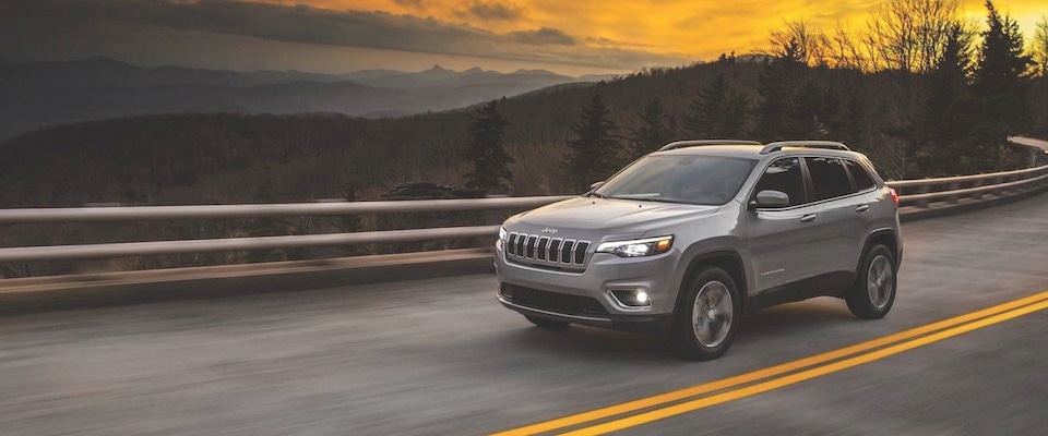 2019 Jeep Cherokee A silver 2019 Jeep Cherokee driving down an open road at sunset
