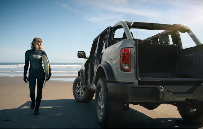 vehicle parked on the beach, with a woman bringing her surfboard to the rear