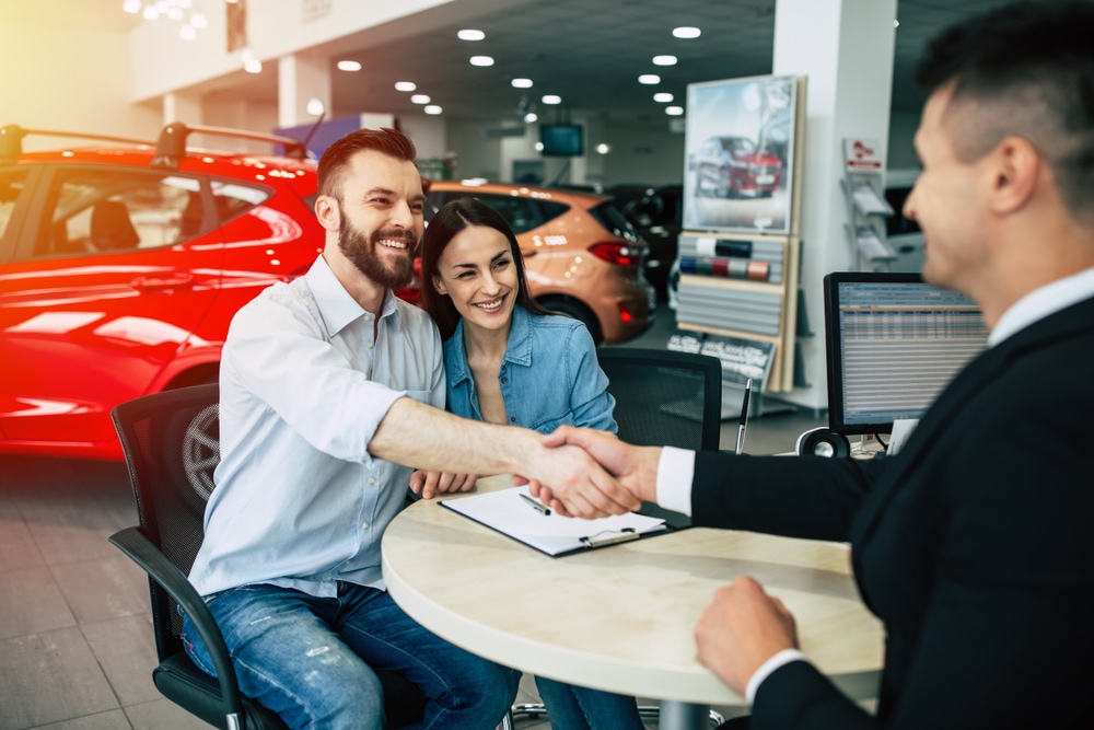 Couple shakes hands with a car salesperson in a dealership, smiling as they finalize their purchase.jpg