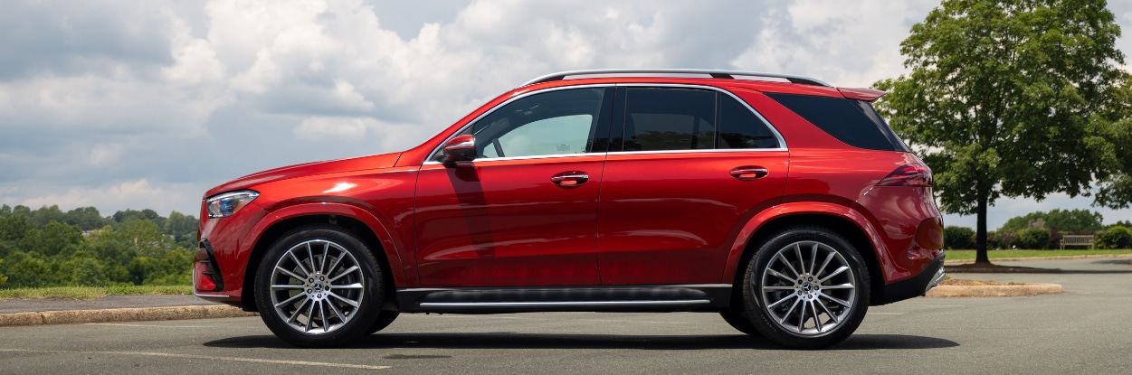 Driver's side view of the exterior of a bright red Mercedes-Benz GLE 450. The SUV is parked and there is a tree line in the background