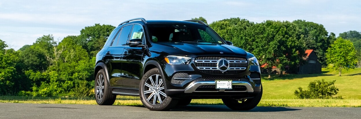 Black Mercedes-Benz SUV facing the camera in front of a green field with trees