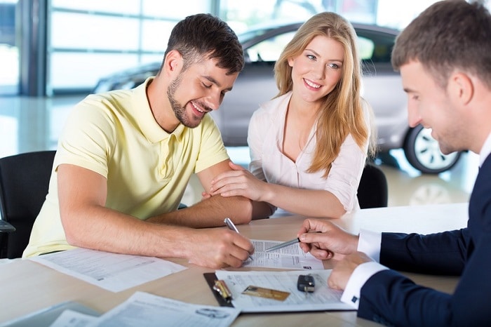 young couple signing paperwork with a car dealer