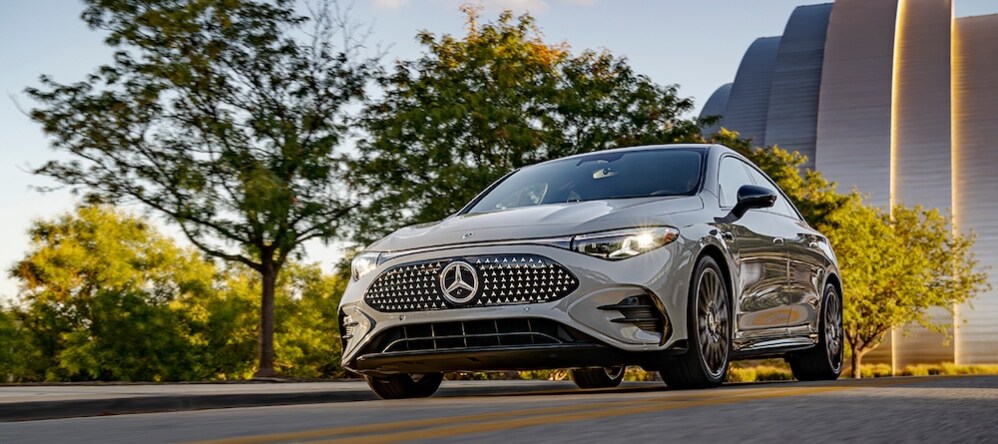 A gray Mercedes-Benz sedan driving down a tree-lined street
