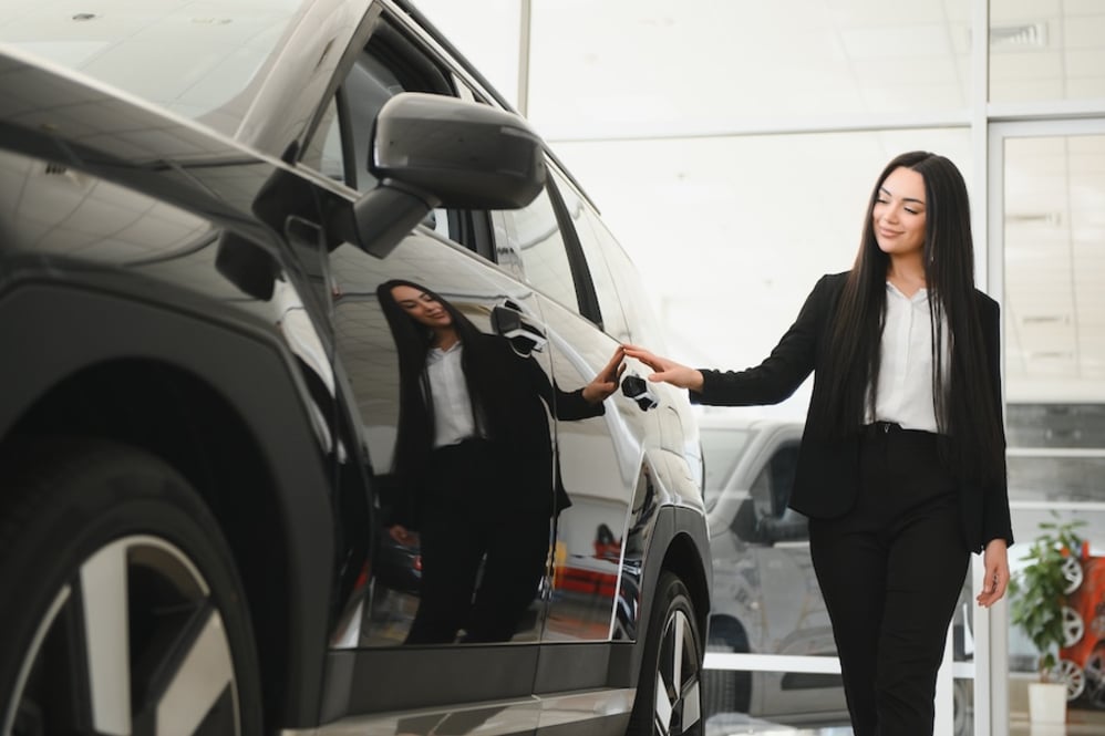A woman in a suit examining a black SUV in a car dealership