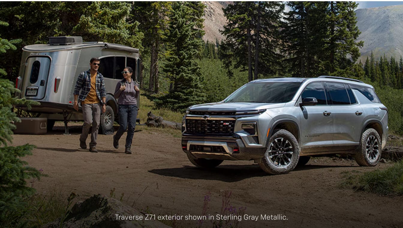 Front three-quarter view of a gray Chevrolet Traverse Z71 towing a small camper.