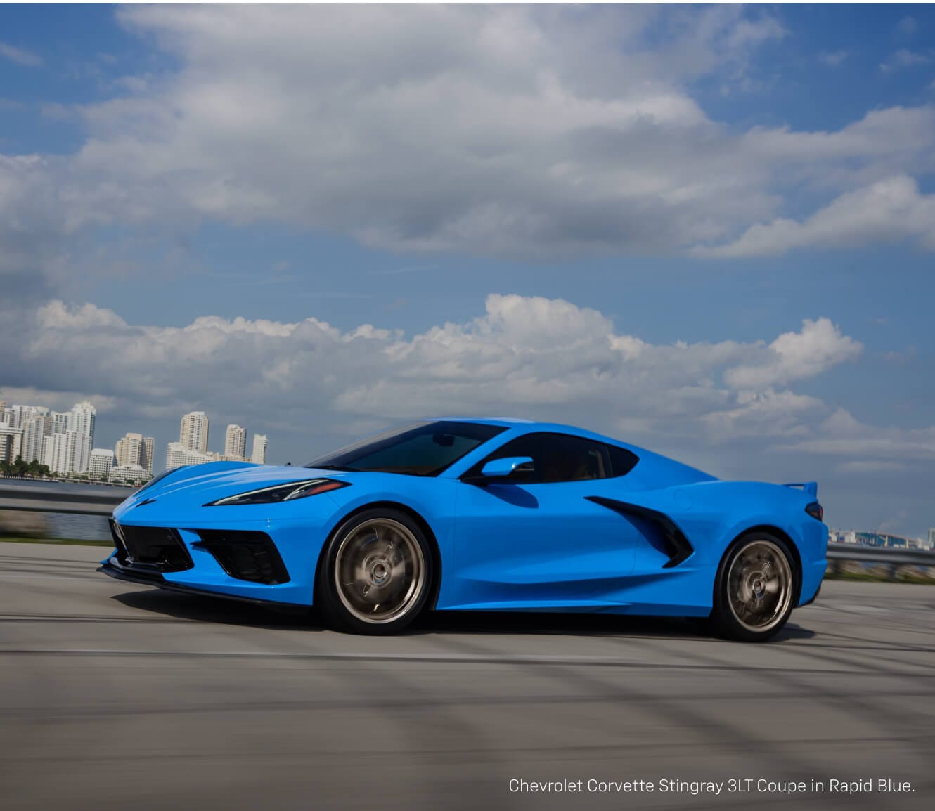 Front quarter view of a Chevrolet Corvette Stingray Coupe in Rapid Blue driving along a coastal highway.