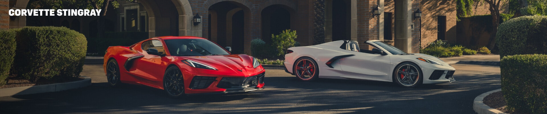 Front view of Chevrolet Corvette Stingray Coupe in Red and Convertible in White parked under palm trees.