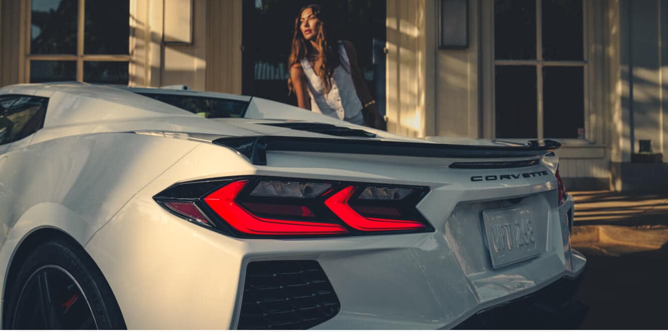 Close-up back view of the Chevrolet Corvette Stingray in Arctic White parked as a woman exits a shop.