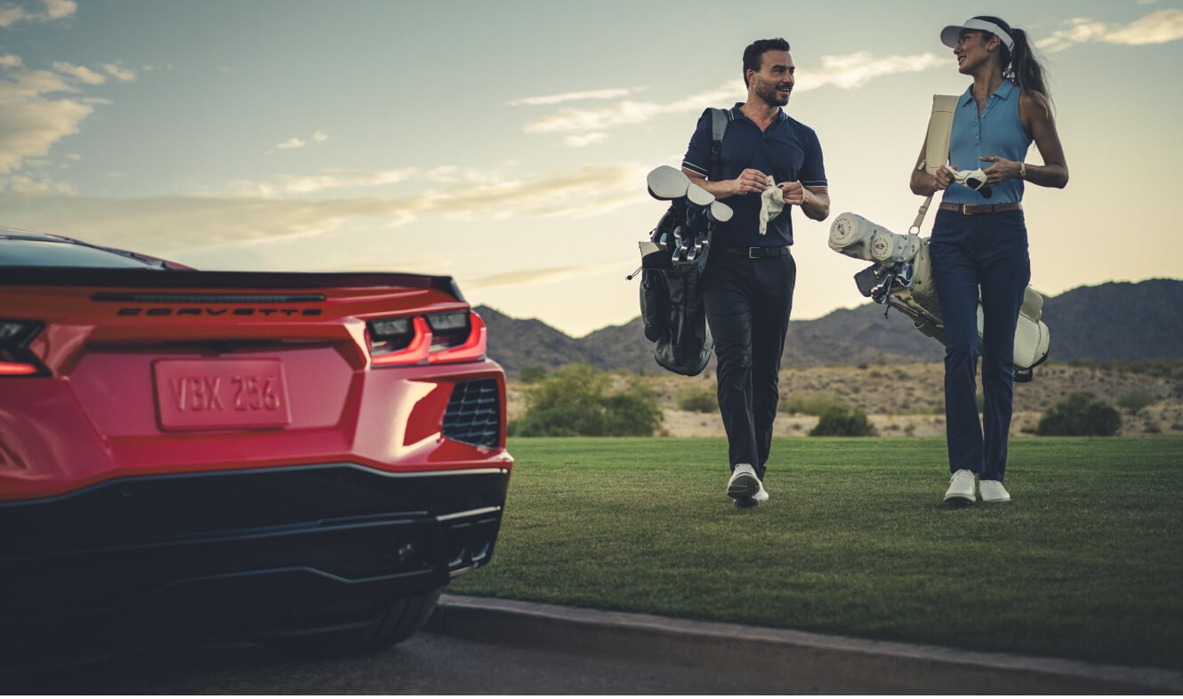 Rear view of a Chevrolet Corvette Stingray in Torch Red parked on a golf course as a couple walks.