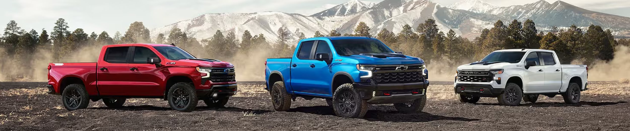Three Chevy trucks parked in front of a mountain backdrop