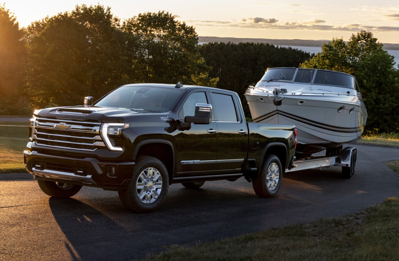 2025 Chevrolet Silverado 2500 Crew Cab HD High Country in Black towing a boat on a sunny day