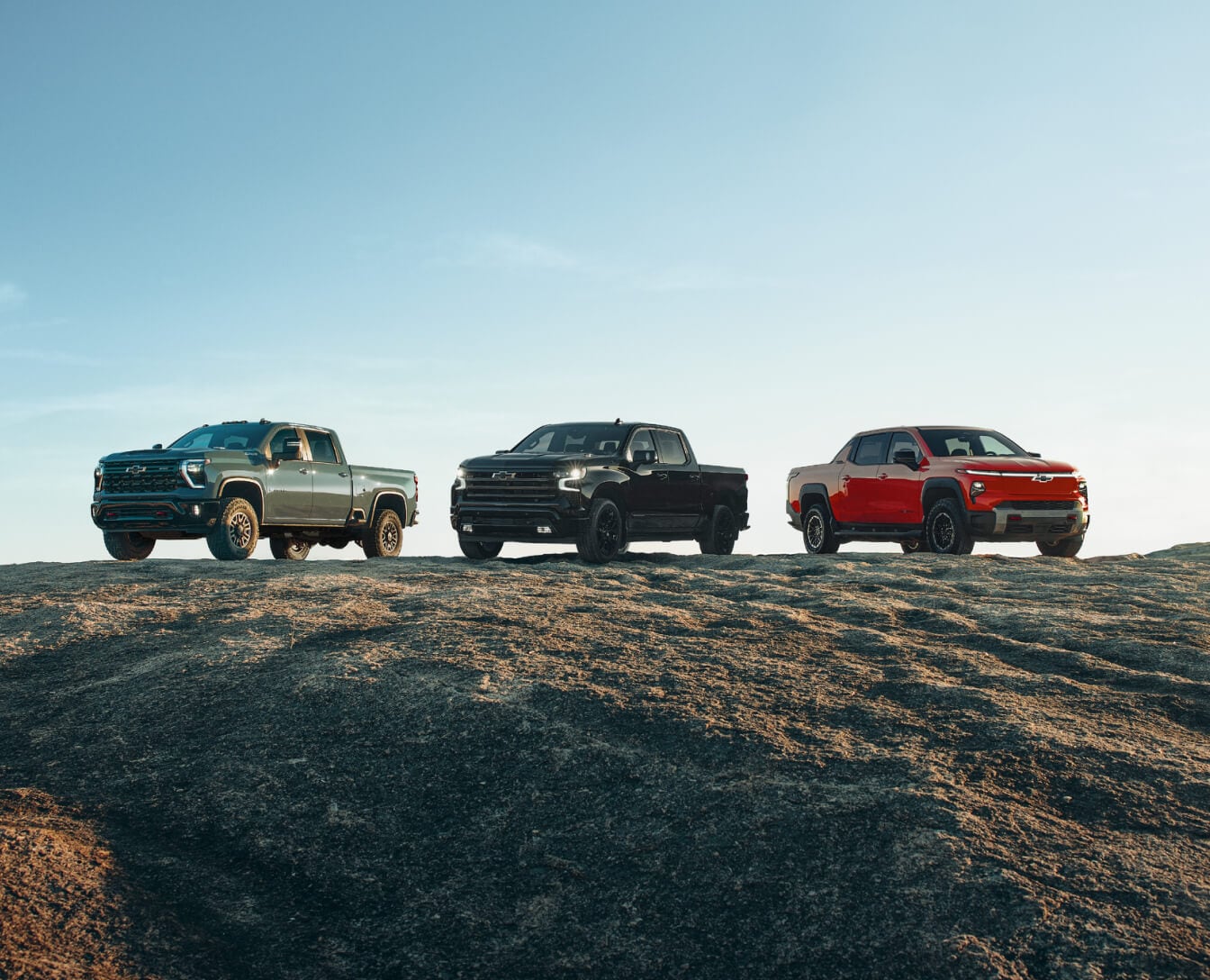 Three Chevrolet Silverado trucks parked atop a dirt hill