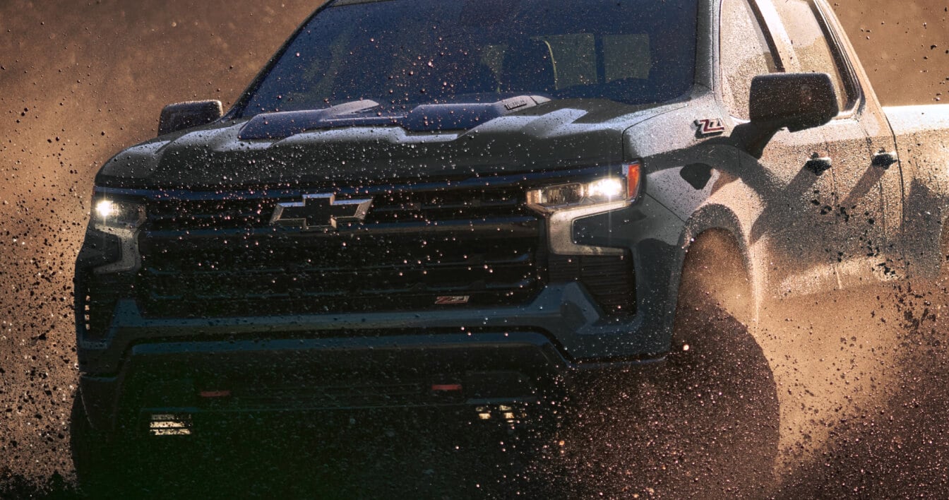 New 2025 Chevy Silverado 1500 Trail Boss in Cypress Gray with RD5 Wheel and 2.7L TurboMax engine off-roading on a sunny day