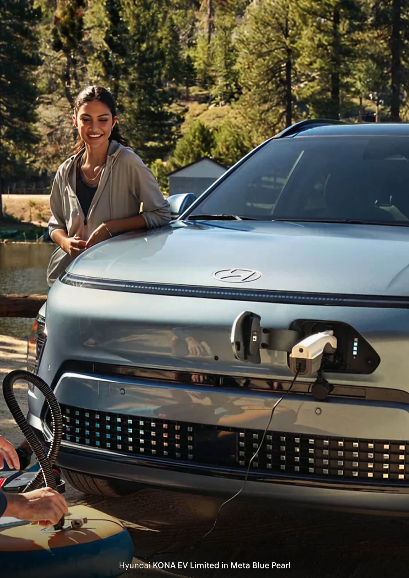 A woman on a camping trip with her Hyundai KONA EV Limited in Meta Blue Pearl