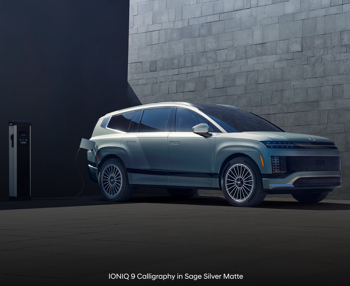 2026 Hyundai IONIQ 9 Calligraphy plugged into a charging station in front of a stone wall