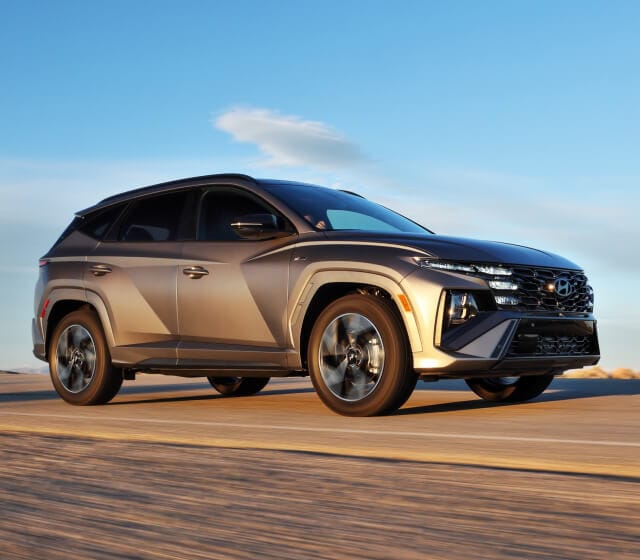 Front quarter tracking view of a Hyundai Tucson in Gray driving down an open desert road.