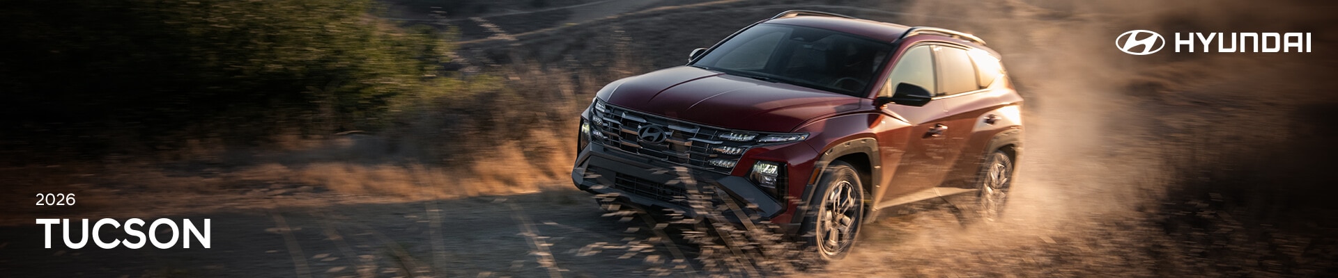 2026 Hyundai Tucson XRT in red driving on a dirt road through a field in the sunlight