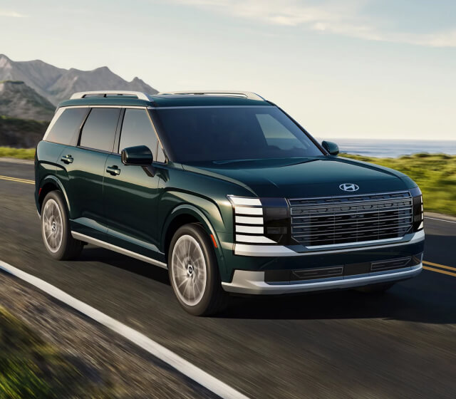 Front quarter view of a Hyundai Palisade Calligraphy in Green driving along a scenic coastal highway.