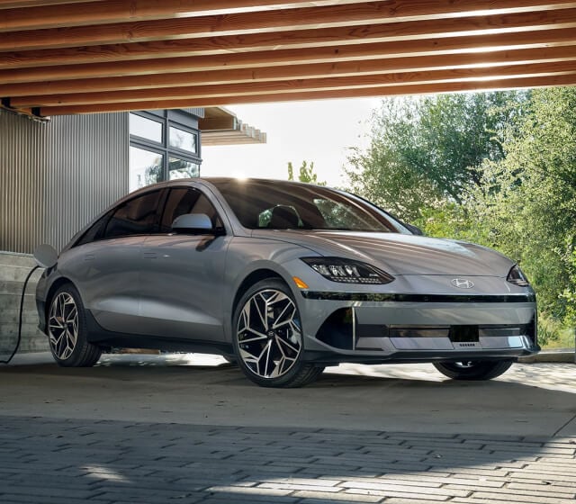 Front quarter view of a Hyundai IONIQ 6 Limited in Silver plugging in a charging cable under a pergola.