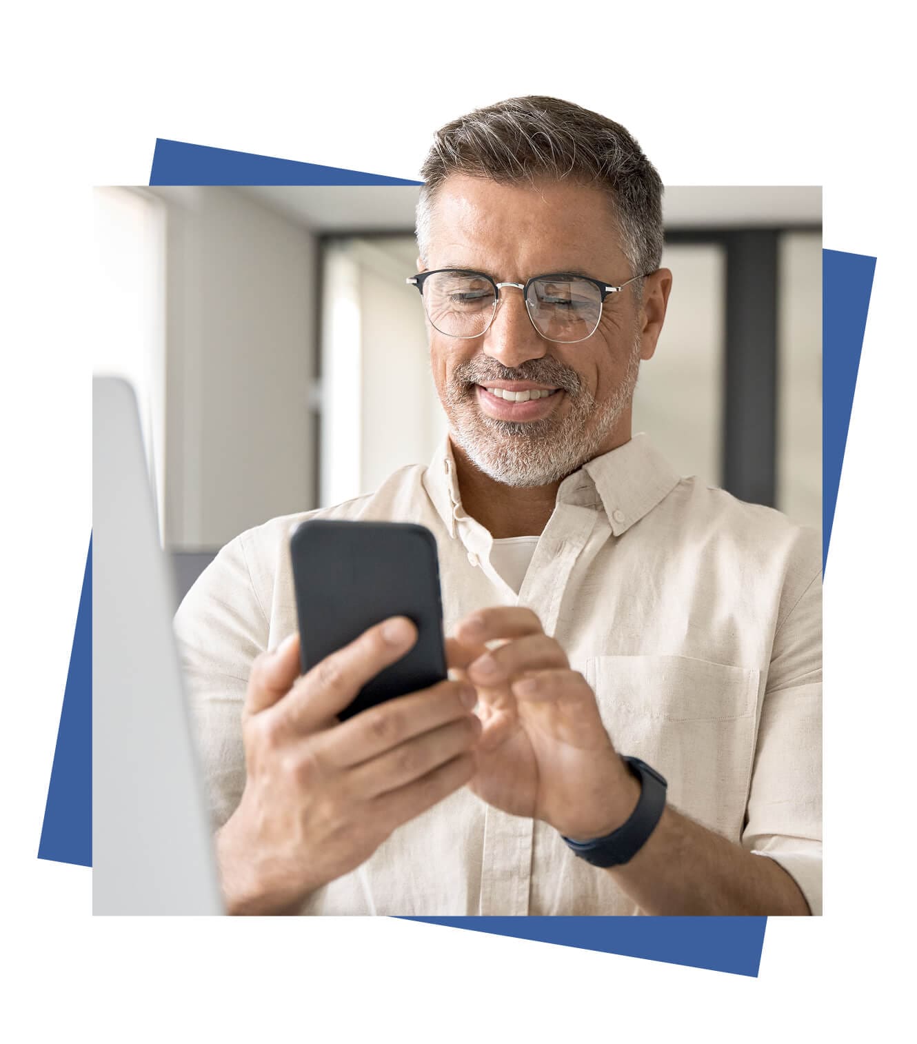 A Man with glasses smiles while using his smartphone in a bright, modern room, conveying a relaxed and content mood