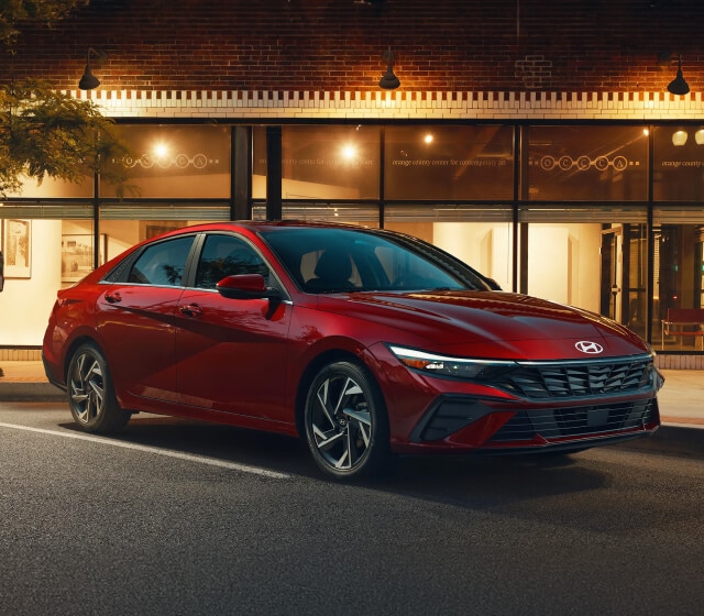Front quarter view of a Hyundai Elantra Limited in Red parked on an urban street at dusk.