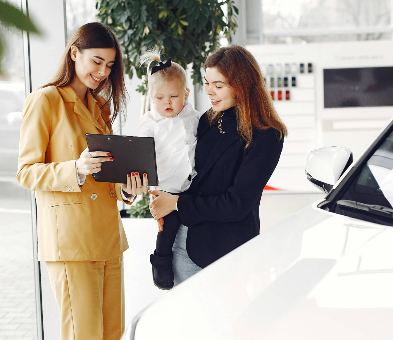 A car saleswoman chatting with a woman and her child next to a new white SUV