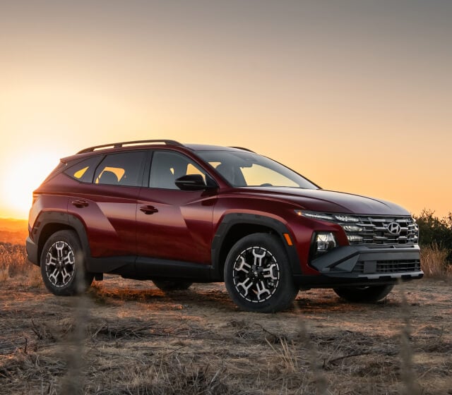 Front quarter view of a Hyundai Tucson XRT in Red parked on a dry dirt field at sunset.