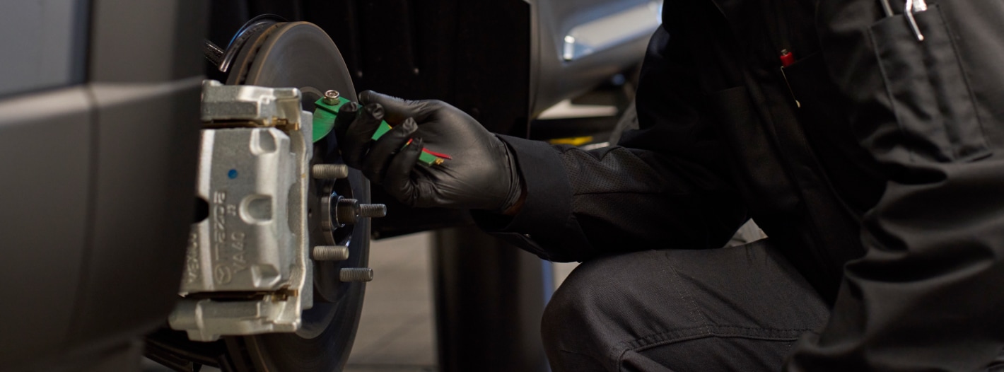 Mazda service technician measuring brake wear with a gauge