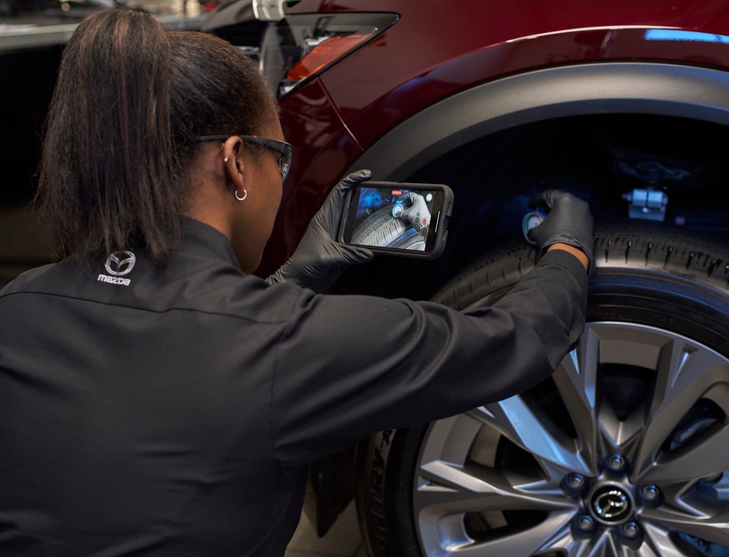 Mazda service technician performing a video inspection on a wheel of a red Mazda