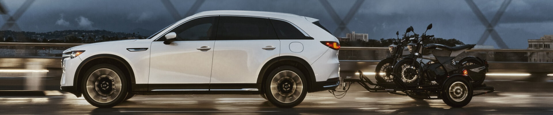 2026 Mazda CX-90 PHEV in Rhodium White towing two scooters over a bridge