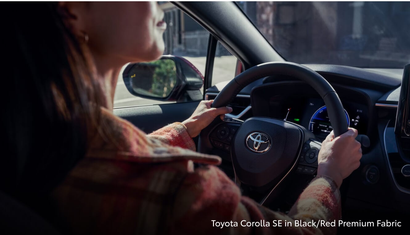 A woman driving and using the touch screen inside of a 2026 Toyota Corolla