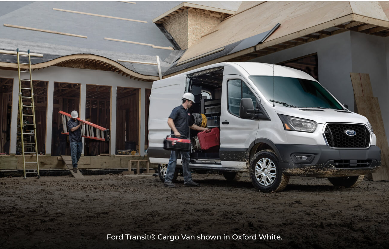 2026 Oxford White Ford Transit Cargo Van parked at a house construction site as construction workers unload tools.