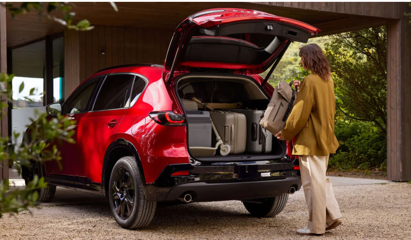Exterior shot showing a Mazda CX-5 with an open tailgate as a woman loads the trunk with luggage.