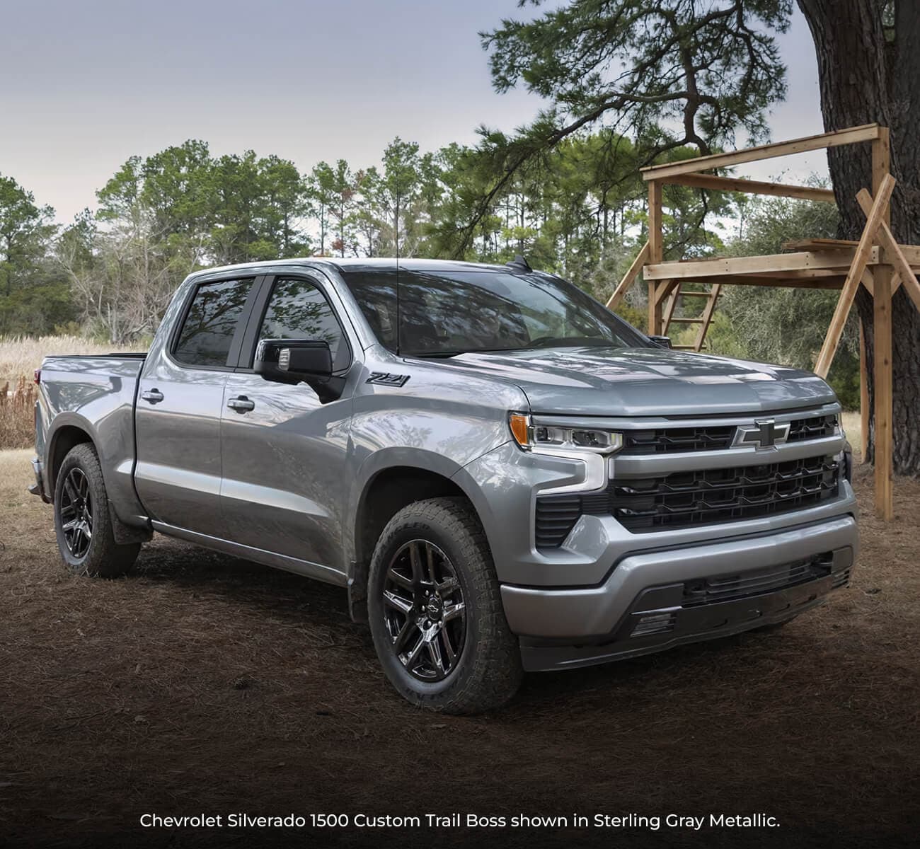 2026 Sterling Gray Metallic Chevrolet Silverado 1500 Custom Trail Boss parked in a field near a wooden treehouse.