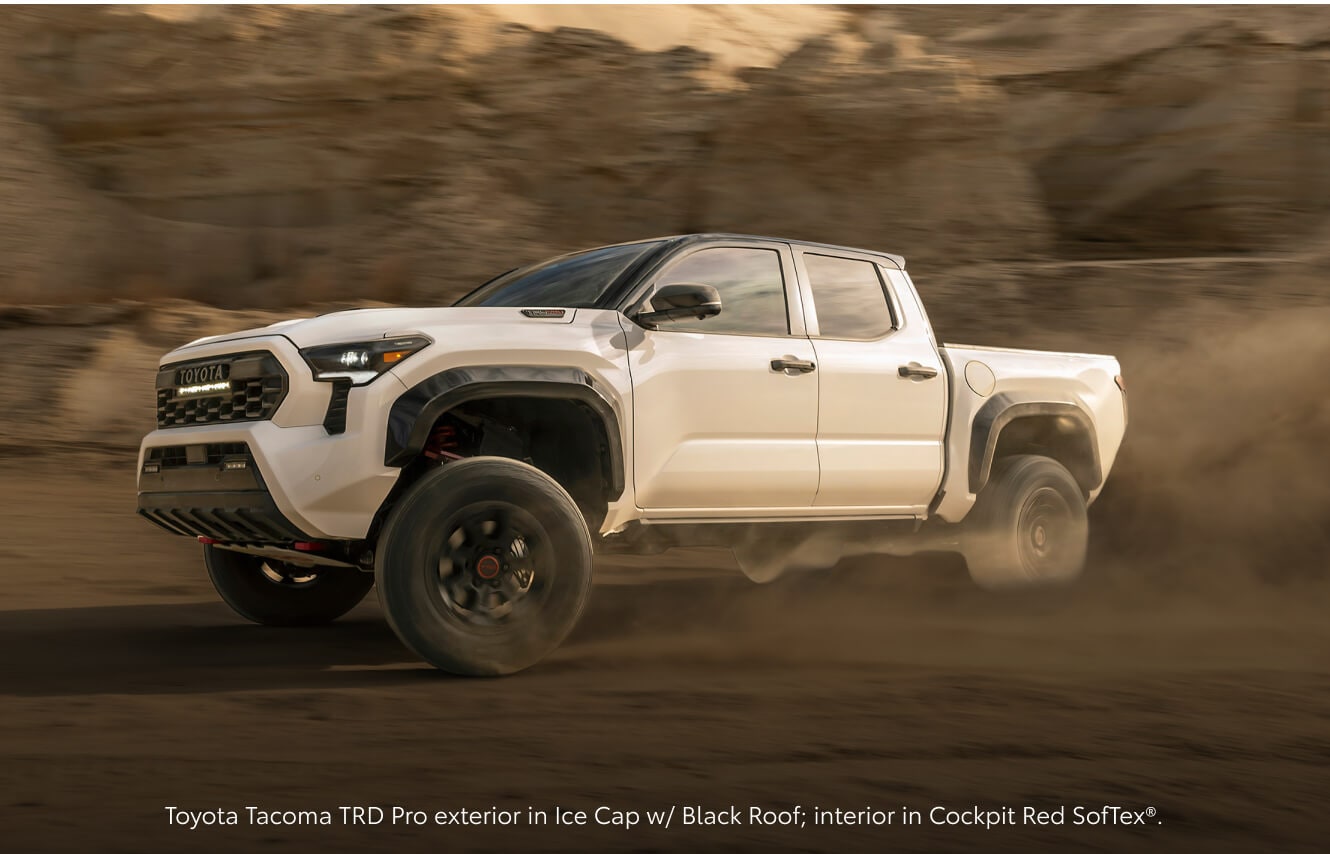 Three-quarter front view of an Ice Cap Toyota Tacoma TRD Pro kicking up dust while speeding.