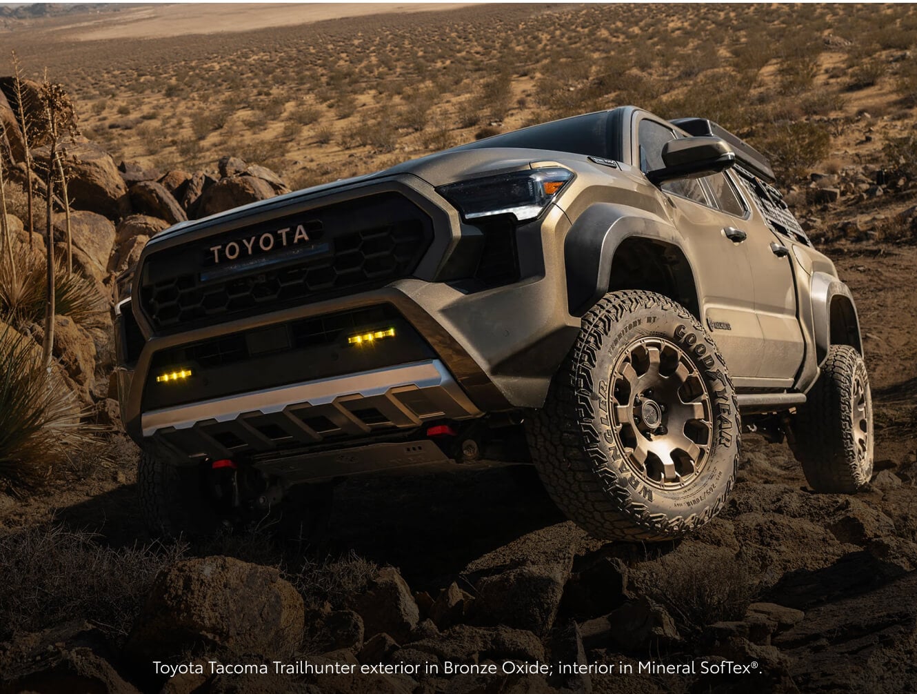 Low-angle front view of a Bronze Oxide Toyota Tacoma Trailhunter navigating rocky terrain.