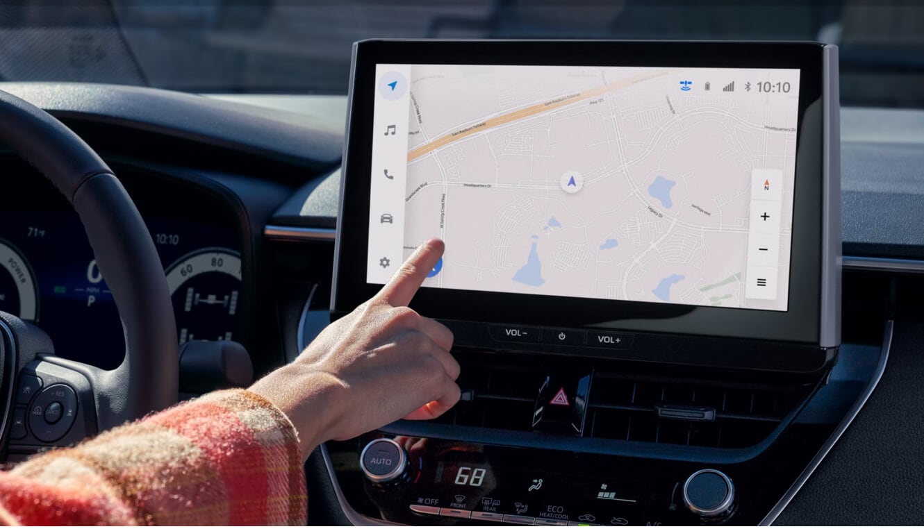 A woman driving and using the touch screen inside of a 2026 Toyota Corolla