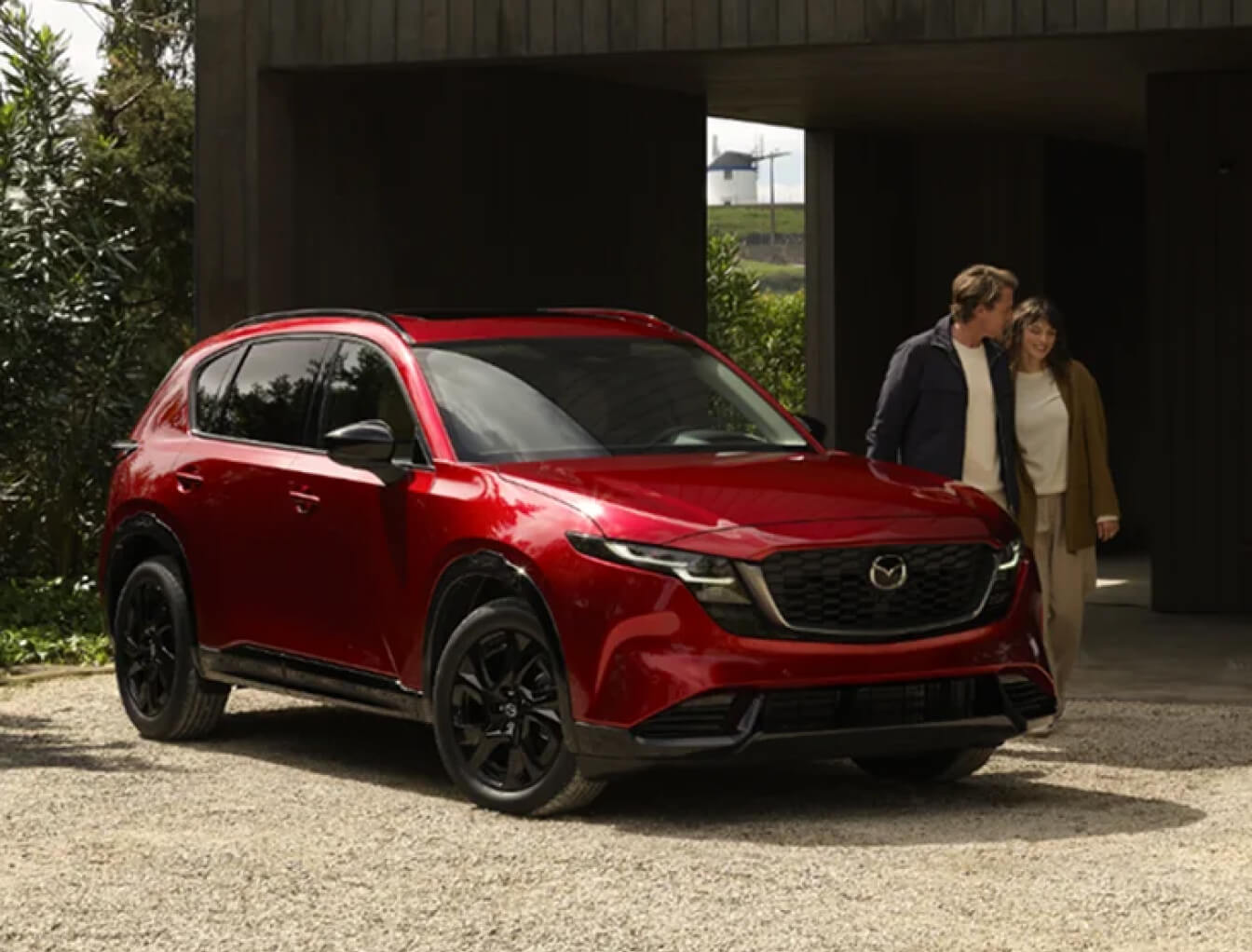 A red 2026 Mazda CX-5 parked in an upscale driveway as a smiling couple walks nearby.