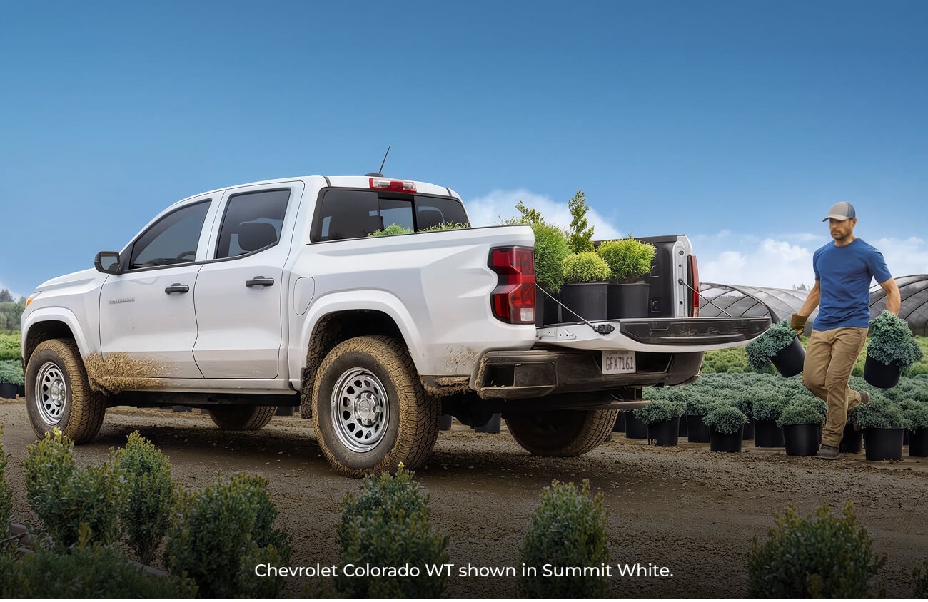2026 Summit White Chevrolet Colorado WT truck parked at a plant nursery as a man carries potted shrubs.