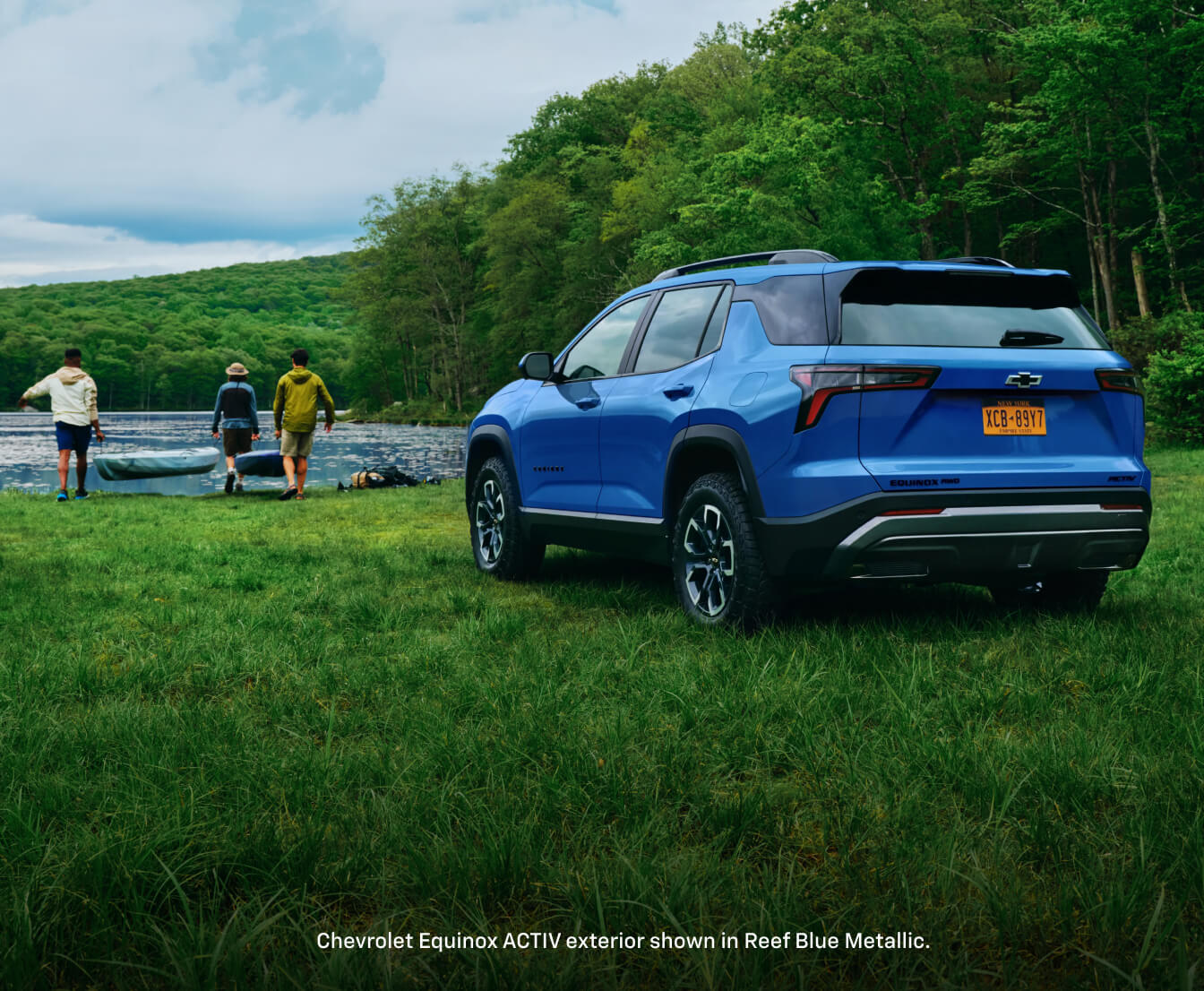 Rear three-quarter view of a 2026 Chevrolet Equinox ACTIV in Reef Blue Metallic parked near people carrying a kayak.