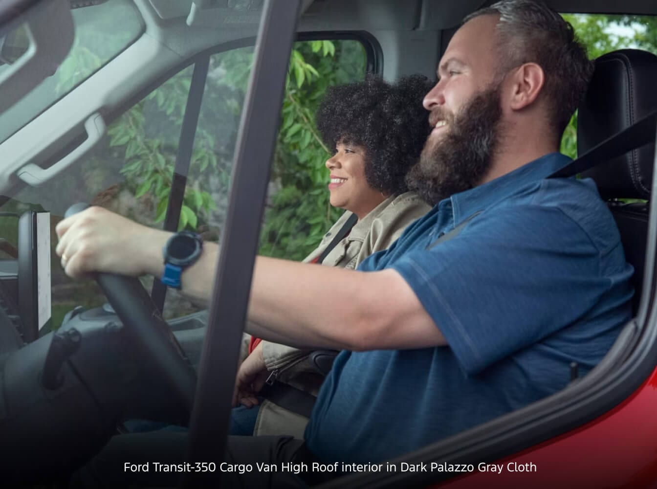 Ford Transit-350 Cargo Van High Roof interior in Dark Palazzo Gray Cloth with driver and passenger smiling inside a red cabin.